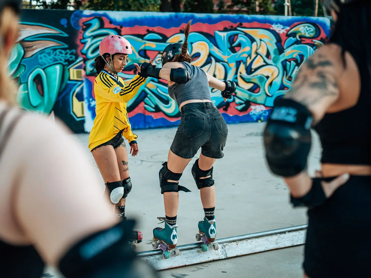 A coach guiding a skater along a rail in front of a graffiti wall