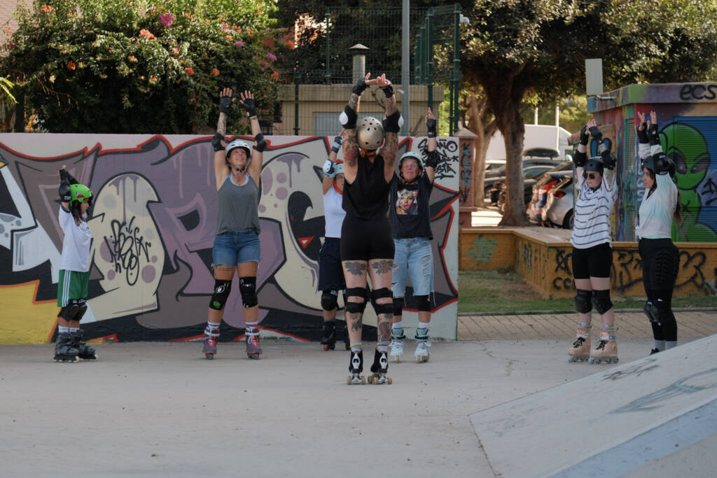 Coach leading a group warm-up with arms raised in front of a graffiti wall