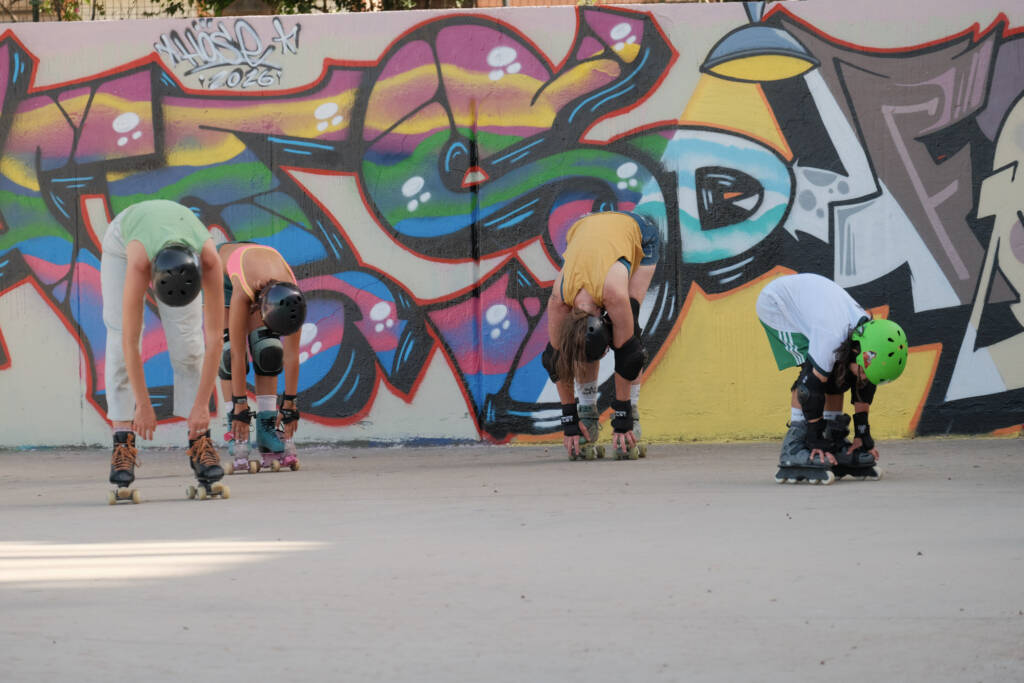 Skaters on quads and inline stretching in front of a colourful graffiti wall